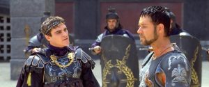 Joaquin Phoenix as Commodus and Russell Crowe as Maximus in a tense scene from Gladiator (2000), wearing Roman armor with guards and shields in the background.
